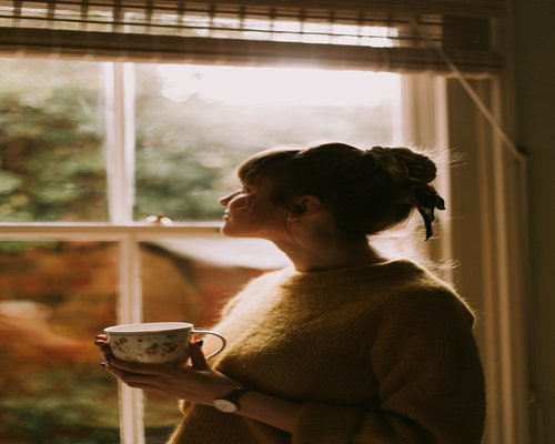Person taking a break with a cup of coffee near a sunny window